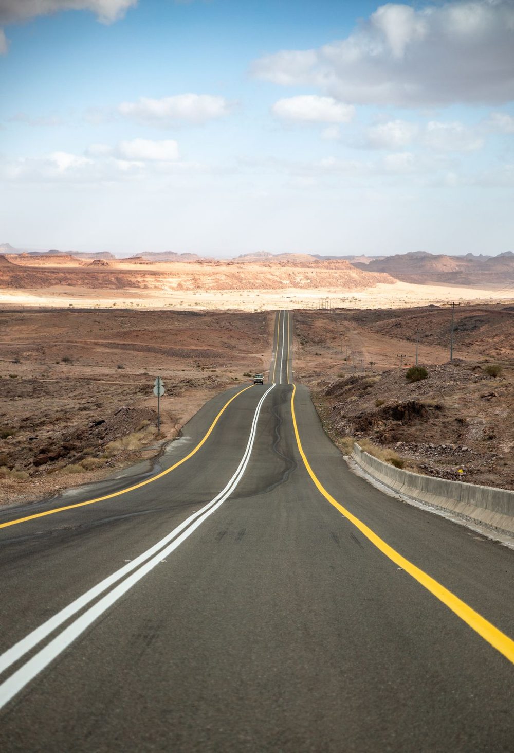 A single car on a remote desert highway under intense sun